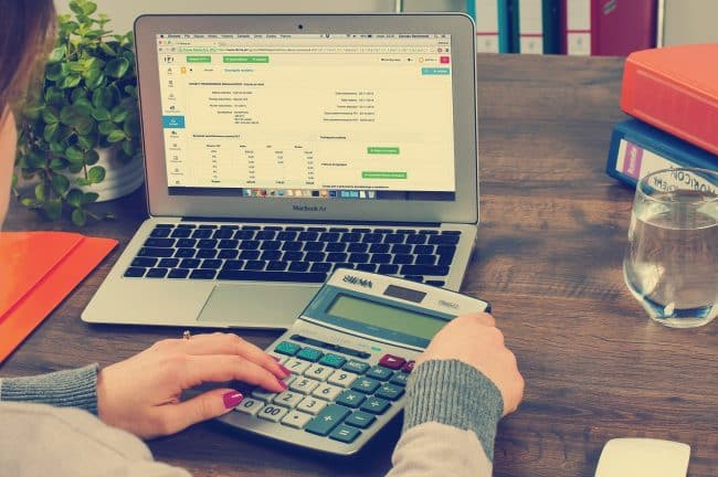 person looking on laptop screen while holding calculator