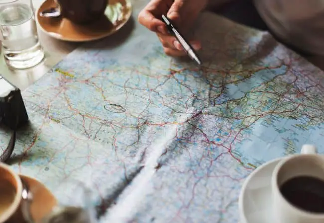 person pointing pen at map while having coffee